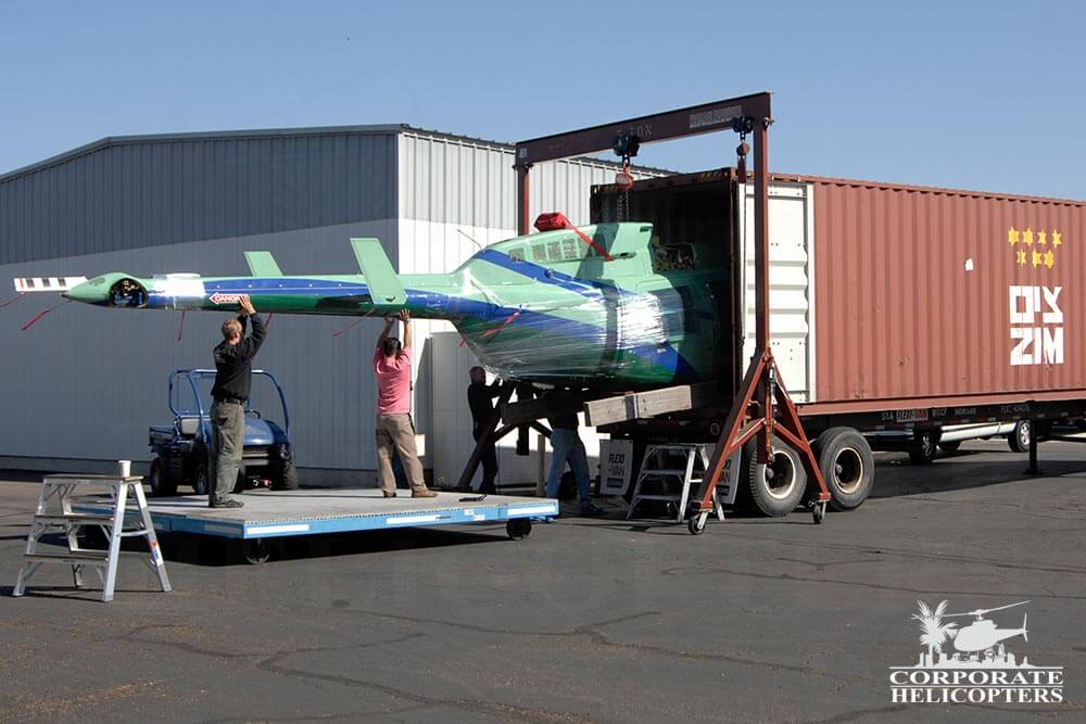 A blue and green helicopter is loaded into a shipping container