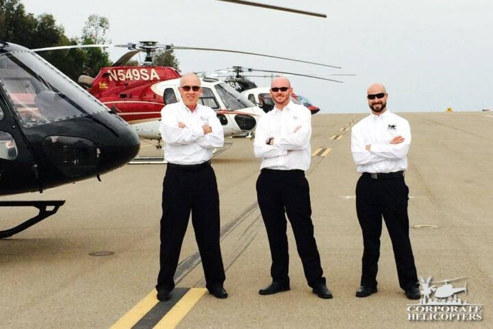 3 Helicopter charter pilots stand in front of their helicopters