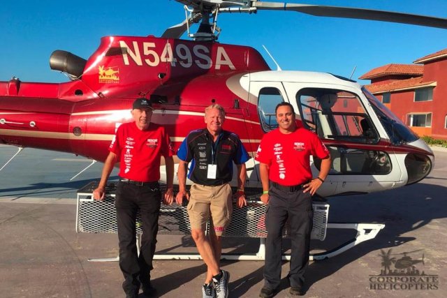 3 men stand in front of a helicopter