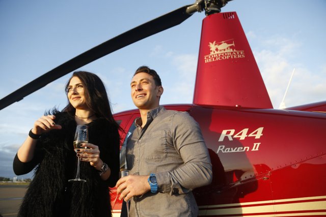A couple poses in front of a helicopter