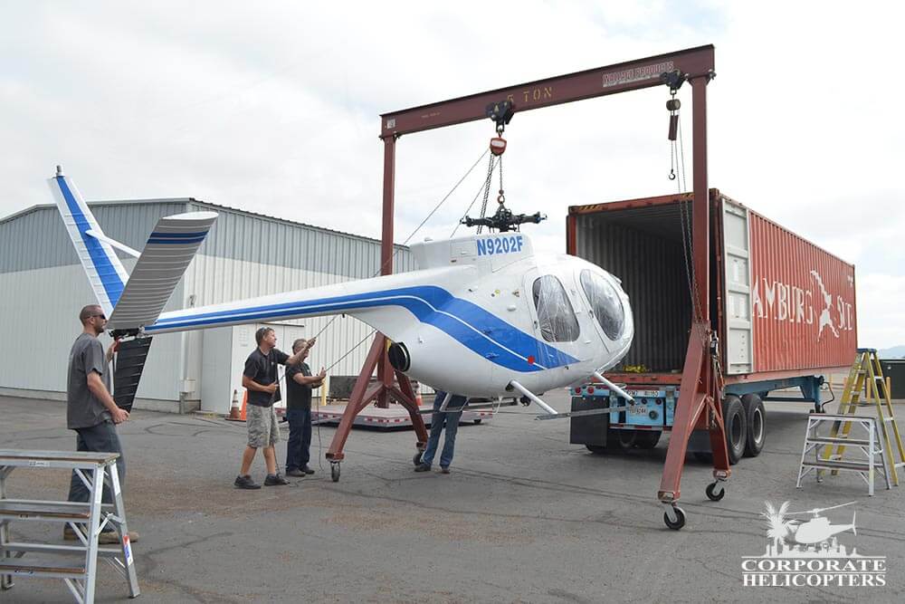 A MD500 helicopter being loaded into a shipping container