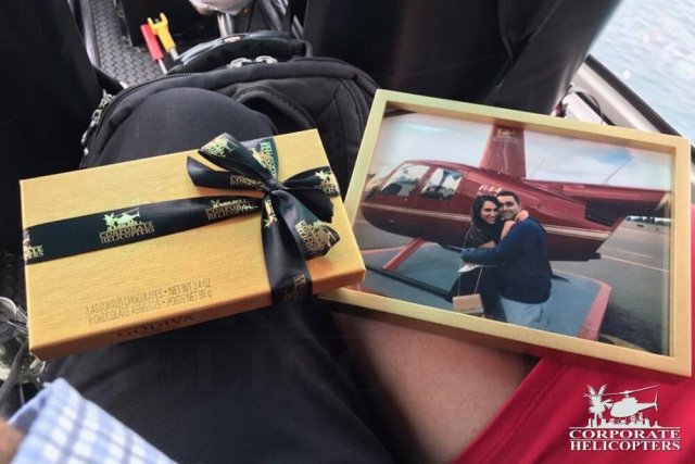 A box of chocolates and a frames photo of a couple sit on the lap of a couple in a helicopter
