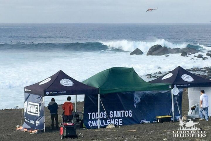 Specatators and event staff view a big wave at the Todos Santos Challenge as a helicopter flies in the distance