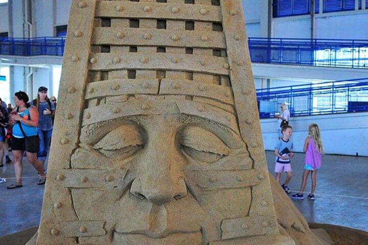 Ornate sand sculpture of a face, people in background