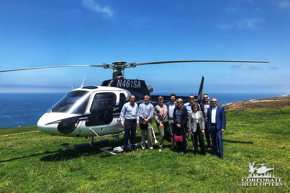 A group of people pose by a helicopter in a grassy field