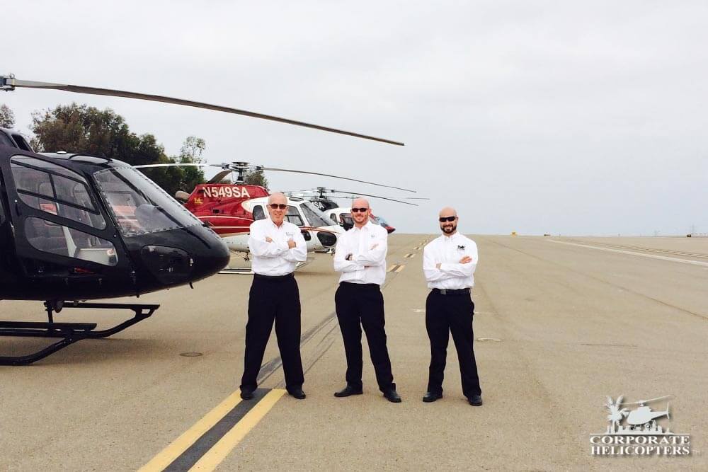 4 pilots stand next to 3 helicopters