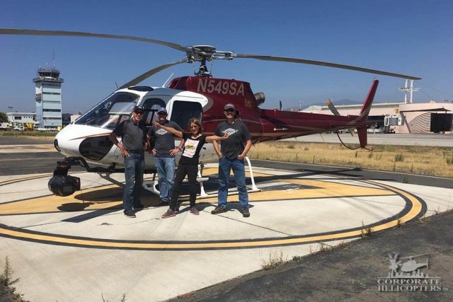 four people stand next to a helicopter