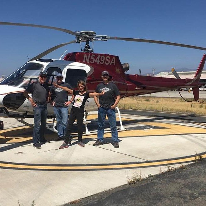 four people stand next to a helicopter