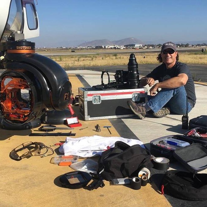 A camera mount, camera gear and cameraman are next to a helicopter