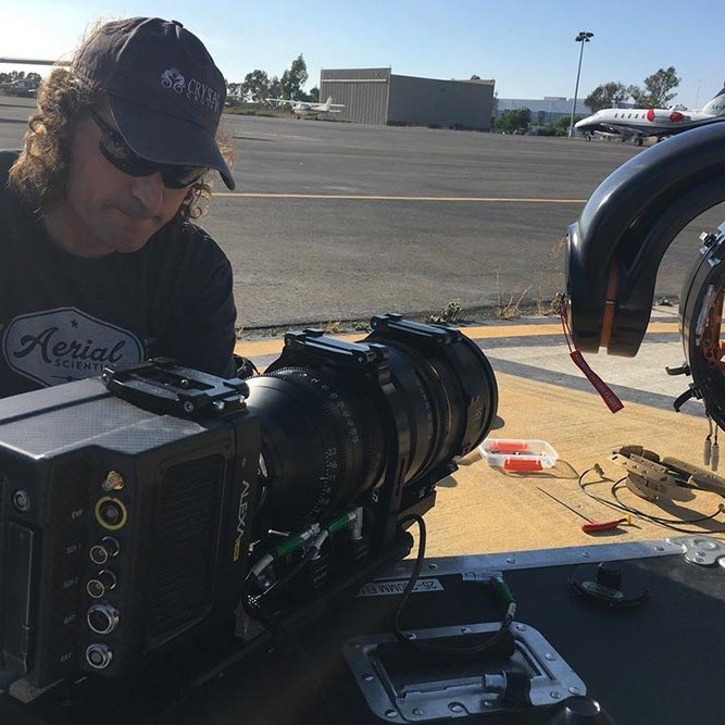 A man works on camera , a helicopter camera mount is next to him