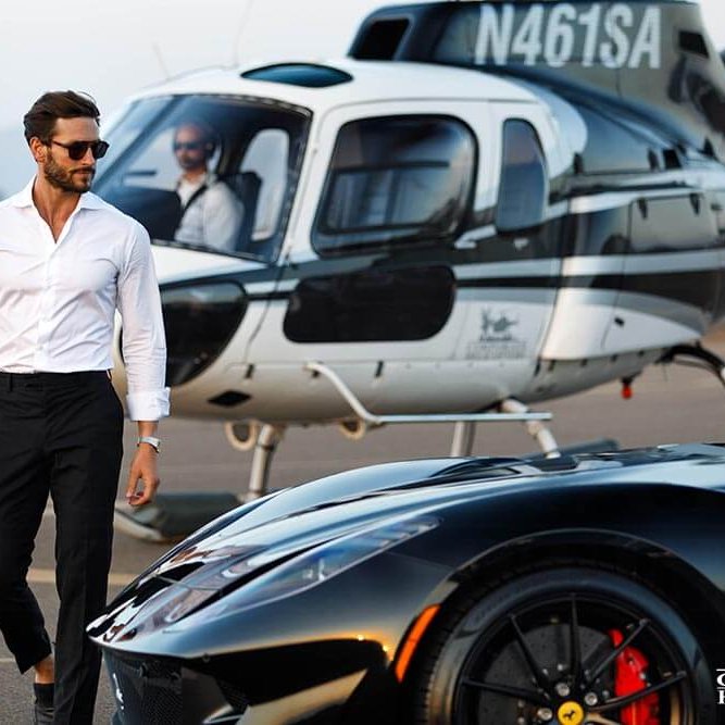 A well-dressed man walks next to a Porsche, a helicopter is in the backgroun