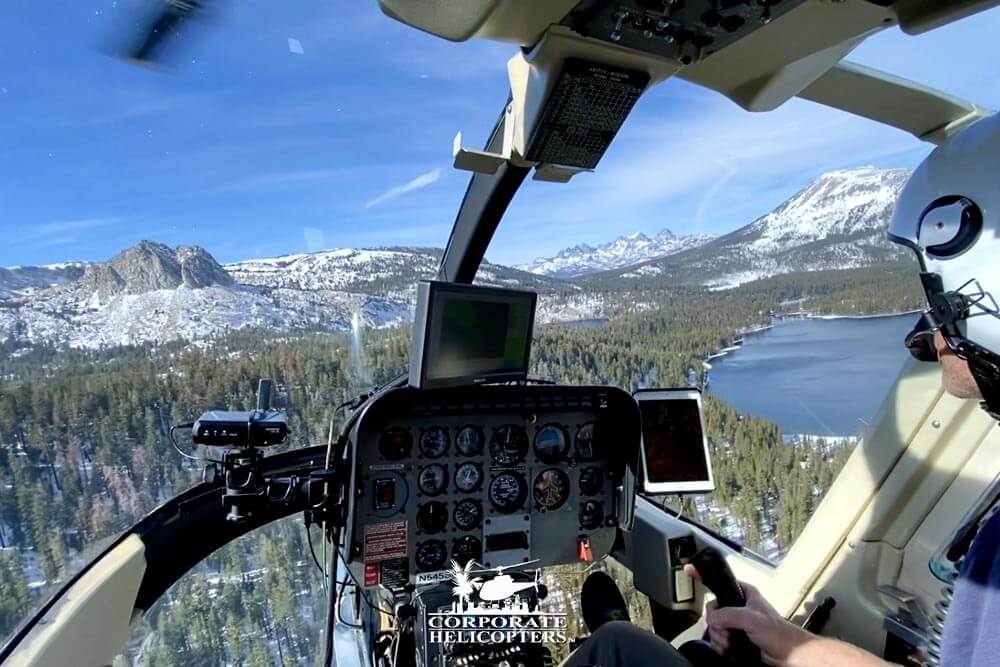 View from helicopter cockpit while flying over forrest and snowy mountains