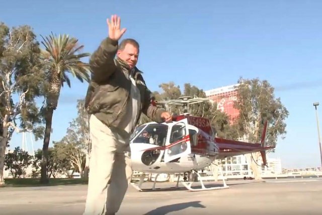William Shatner waves to the camera as he walks toward a helicopter