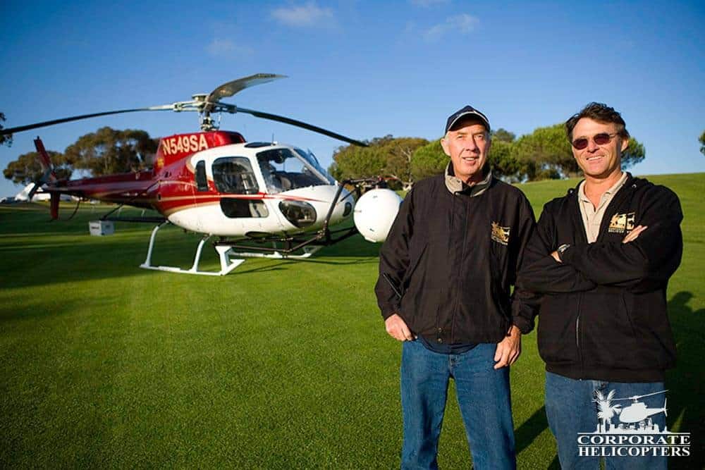 Two men stand in front of a helicopter on a golf course