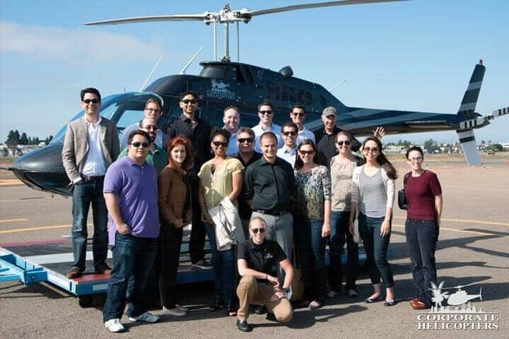 A large group of people pose in front of a helicopter