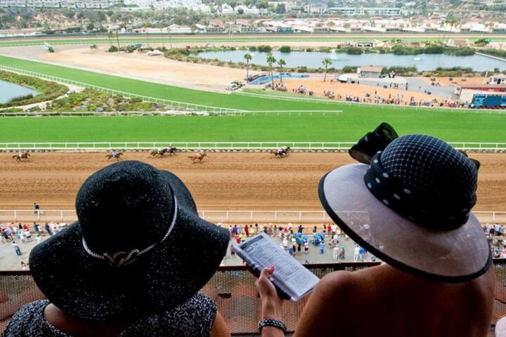 Two women in fancy hats watch horse race at Del Mar Thoroughbred Club