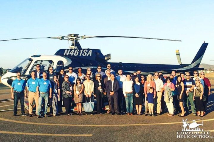 A group of about 30 people pose in front of a helicopter