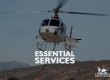 Helicopter with cargo basket and long line attached. Text overlay reads: Essential Services