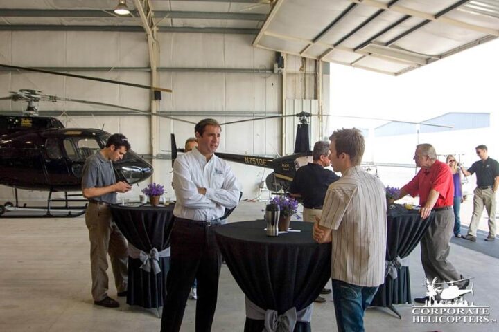 People talking around a few decorated tables in a helicopter hangar bay