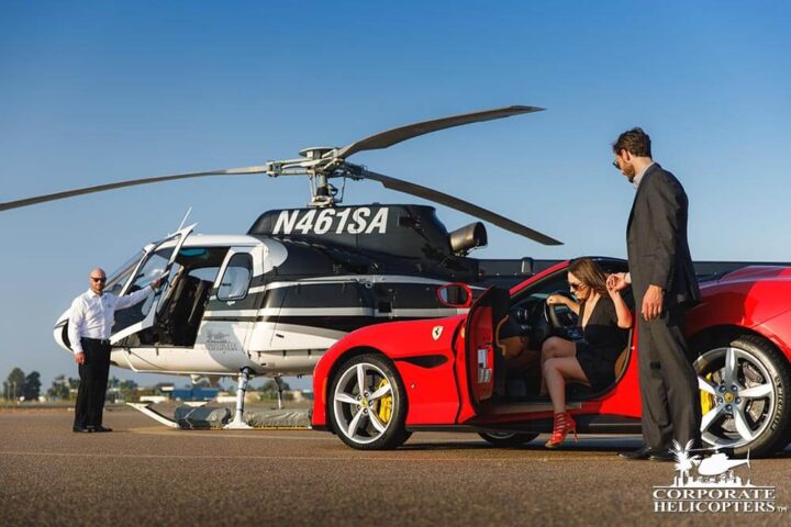 Man helps woman exit Porsche with helicopter waiting for them in the background