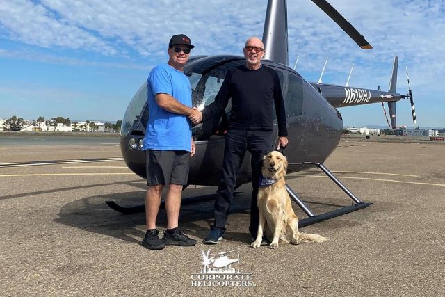 Jim McCoy shakes Ivor Shier's hand in front of a new Robinson R44 Raven Il. A dog sits next to Ivor.