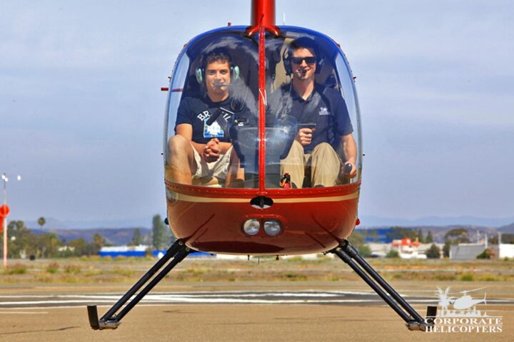 Two people in a helicopter. The helicopter is hovering inches from the ground.