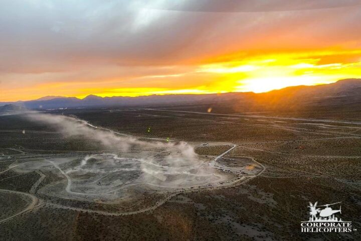 Aerial photo of a sunset, below that a group of off-road cars make dust trails.
