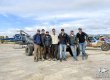 Off road race crews posing for photograph in front of race vehicles and helicopter