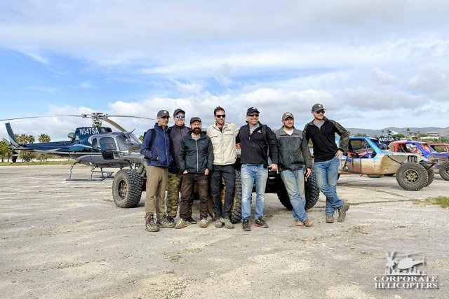 Off road race crews posing for photograph in front of race vehicles and helicopter