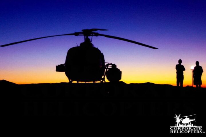 A helicopter and two people silouetted against a sunset