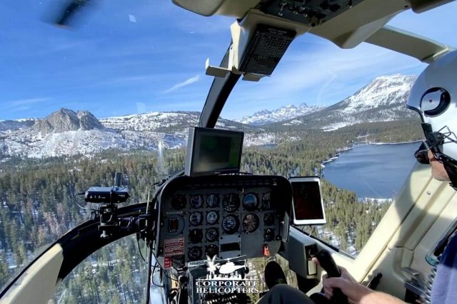 View from helicopter cockpit while flying over forrest and snowy mountains