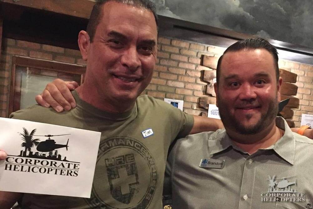 Two men pose for a photo, one holds up a paper with the Corporate Helicopters logo on it