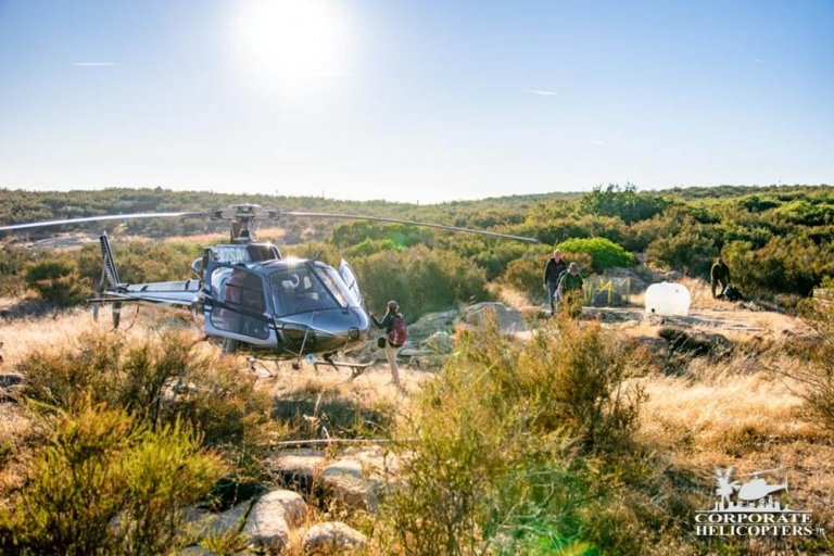 A woman stands next to a helicopter parked in a small field, 3 other people approach