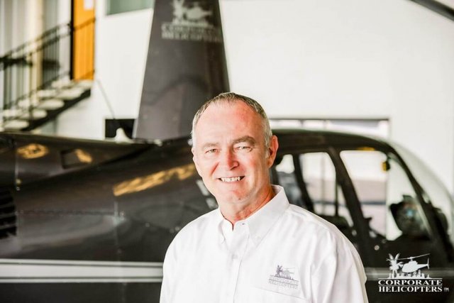 Captain Terry Frost smiles, a Robinson helicopter is in the background